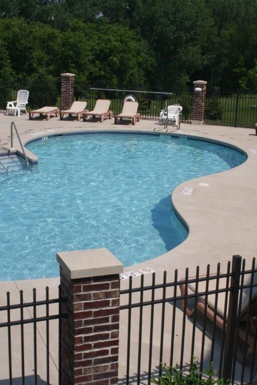 Outdoor pool with lounge chairs behind a brick and iron fence